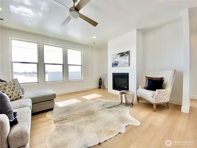 living room with recessed lighting, light wood-style flooring, a glass covered fireplace, ceiling fan, and baseboards