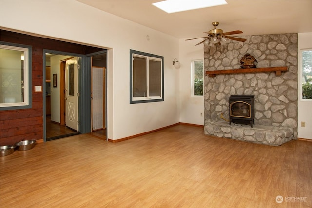 unfurnished living room featuring a wood stove, light hardwood / wood-style flooring, and ceiling fan