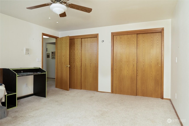 unfurnished bedroom featuring light carpet, ceiling fan, and two closets