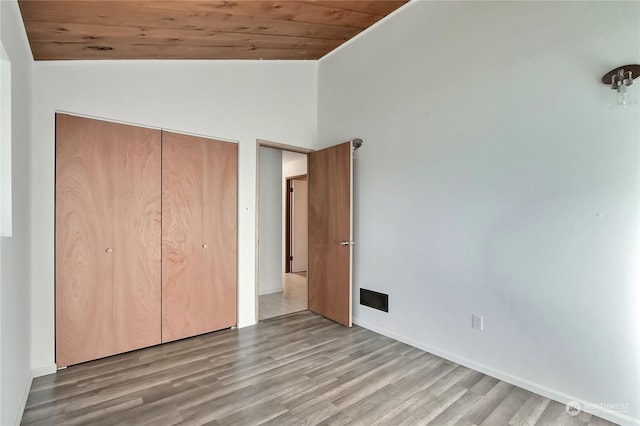 unfurnished bedroom featuring lofted ceiling, light hardwood / wood-style floors, wooden ceiling, and a closet