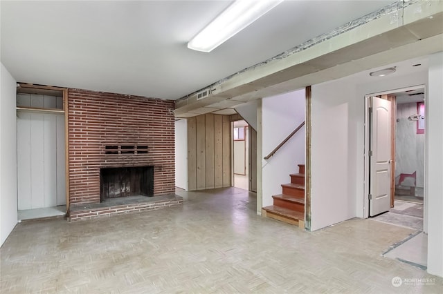 unfurnished living room with wood walls, light parquet flooring, and a brick fireplace