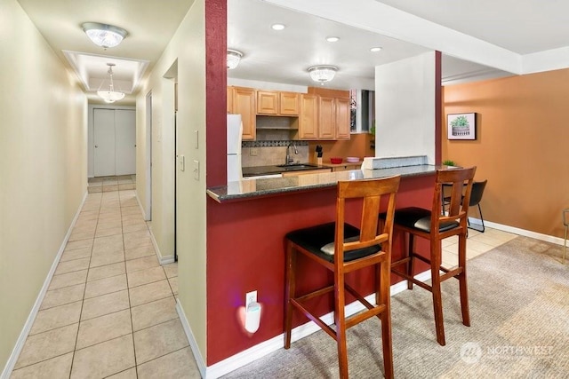 kitchen with a kitchen breakfast bar, tasteful backsplash, kitchen peninsula, dark stone countertops, and white fridge