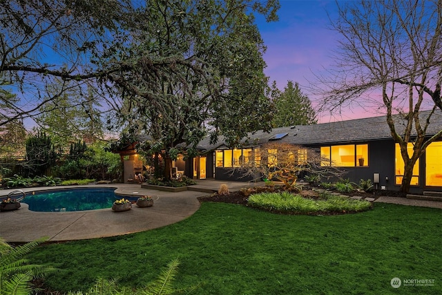 pool at dusk featuring a lawn and a patio