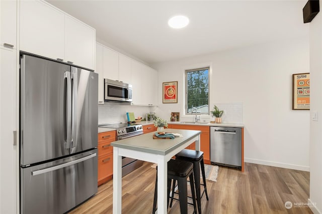 kitchen with backsplash, white cabinets, sink, light wood-type flooring, and stainless steel appliances