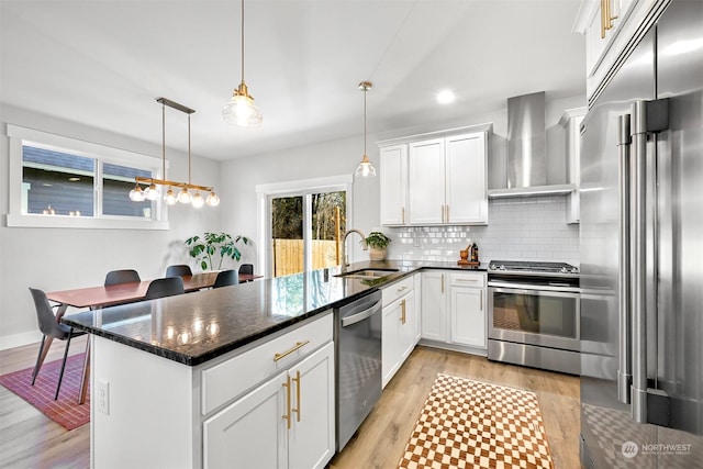 kitchen with pendant lighting, wall chimney range hood, sink, white cabinetry, and stainless steel appliances