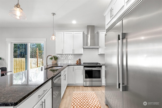 kitchen featuring decorative light fixtures, sink, stainless steel appliances, and wall chimney range hood