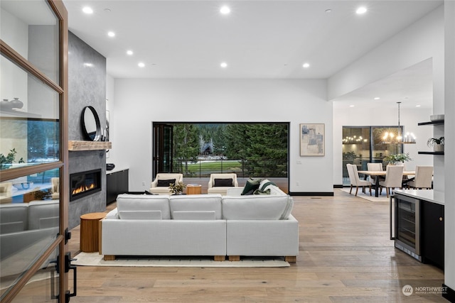 living room featuring wine cooler, a large fireplace, a chandelier, and light wood-type flooring