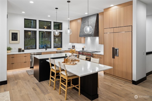 kitchen featuring stainless steel appliances, wall chimney range hood, decorative light fixtures, a kitchen bar, and a kitchen island