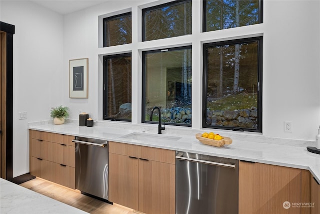 kitchen featuring light stone counters, dishwasher, sink, and light hardwood / wood-style flooring