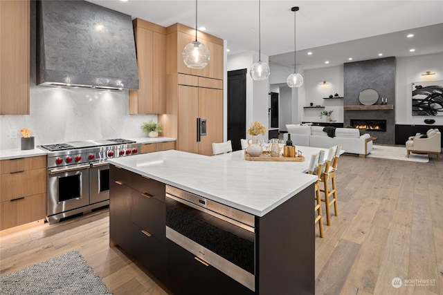 kitchen with wall chimney range hood, light hardwood / wood-style flooring, decorative light fixtures, high quality appliances, and a kitchen island