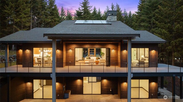 back house at dusk featuring solar panels and a balcony