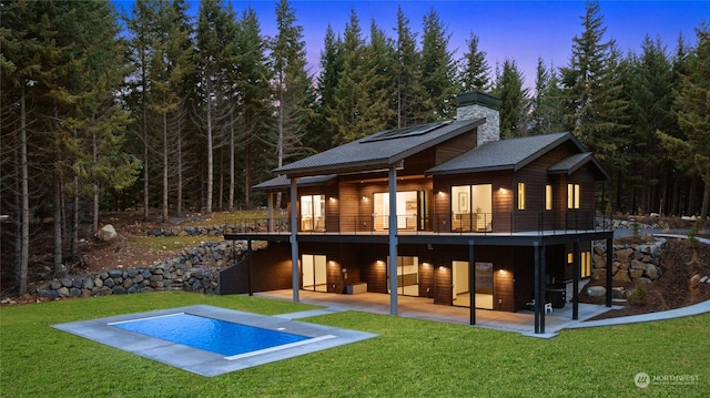 back house at dusk featuring a swimming pool side deck, a patio, and a lawn