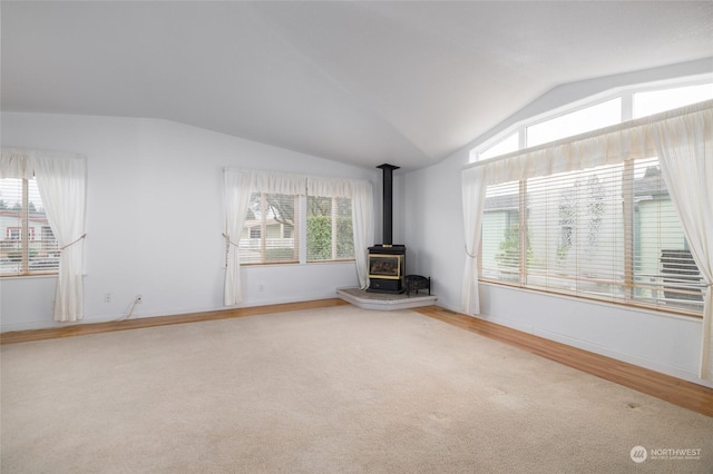 unfurnished living room featuring carpet flooring, a wood stove, and lofted ceiling