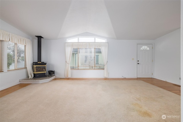 unfurnished living room with a wood stove, carpet floors, and lofted ceiling