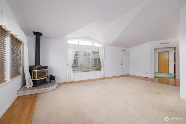 unfurnished living room featuring vaulted ceiling, carpet floors, and a wood stove