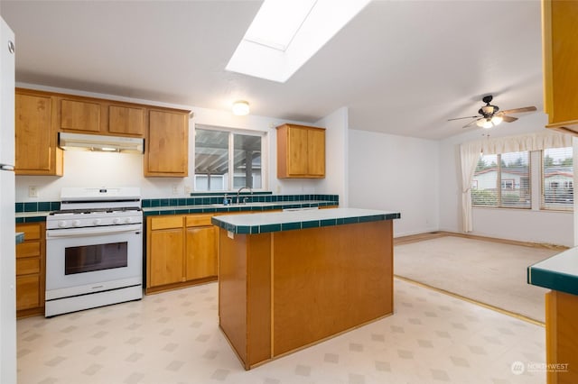 kitchen with a skylight, ceiling fan, white gas stove, tile countertops, and a kitchen island