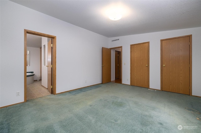 unfurnished bedroom featuring two closets, ensuite bathroom, vaulted ceiling, a textured ceiling, and light colored carpet