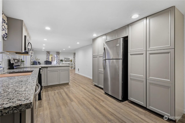 kitchen featuring kitchen peninsula, appliances with stainless steel finishes, gray cabinetry, sink, and light hardwood / wood-style flooring