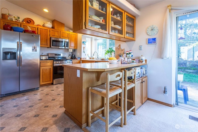 kitchen featuring lofted ceiling, sink, appliances with stainless steel finishes, a kitchen bar, and kitchen peninsula