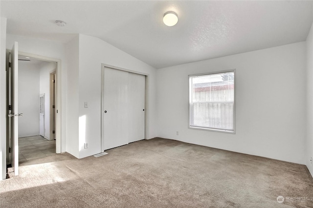 unfurnished bedroom featuring a textured ceiling, light colored carpet, vaulted ceiling, and a closet