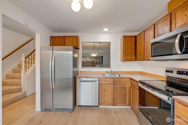 kitchen with stainless steel appliances, light hardwood / wood-style floors, sink, and hanging light fixtures