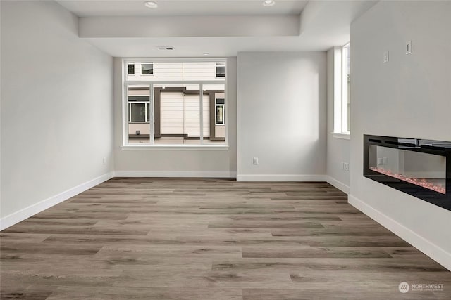 unfurnished living room with a glass covered fireplace, recessed lighting, baseboards, and wood finished floors