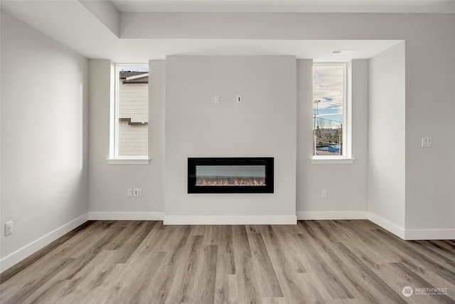 unfurnished living room with wood finished floors, a glass covered fireplace, and baseboards