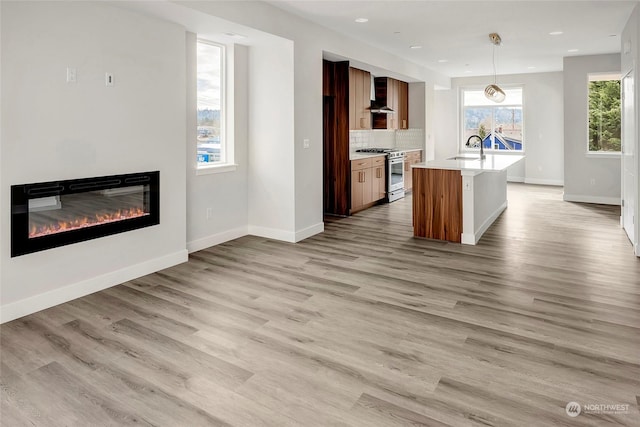 kitchen featuring high end stainless steel range, sink, decorative light fixtures, a kitchen island with sink, and wall chimney range hood