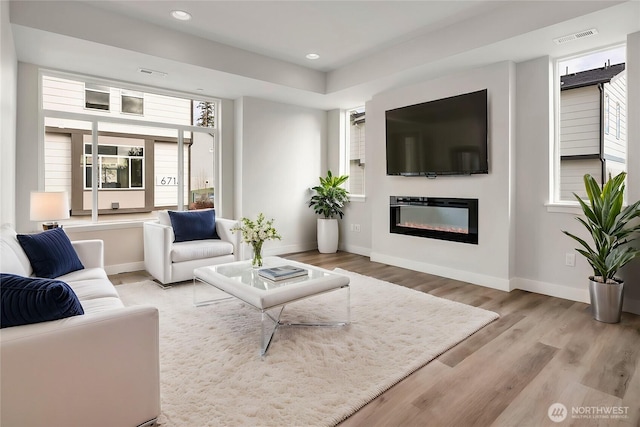 living area with wood finished floors, a glass covered fireplace, visible vents, and baseboards