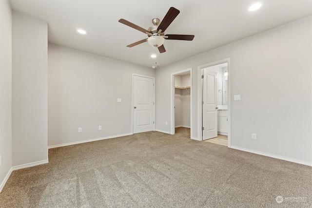 unfurnished bedroom featuring light carpet, a walk in closet, a closet, and ceiling fan