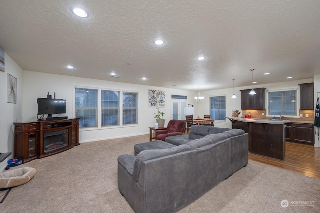 living room featuring light carpet, a textured ceiling, an inviting chandelier, and sink