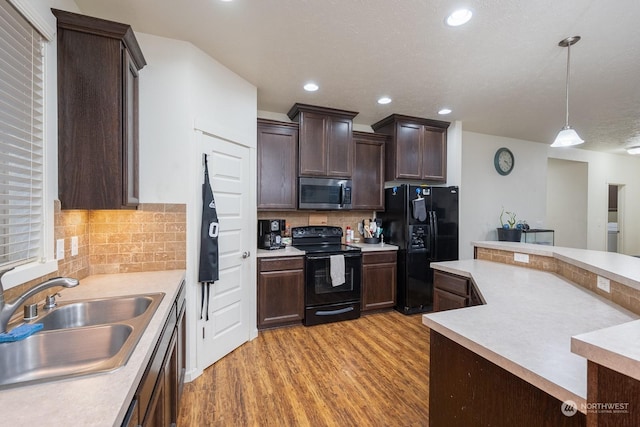 kitchen featuring sink, backsplash, pendant lighting, light hardwood / wood-style floors, and black appliances