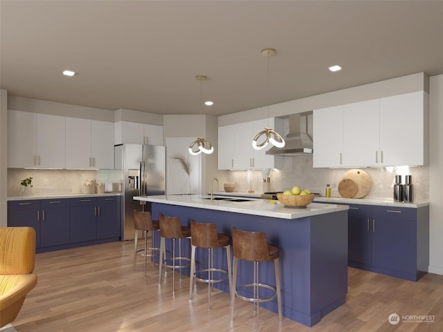 kitchen with white cabinets, wall chimney exhaust hood, hanging light fixtures, and a center island with sink