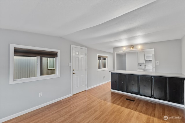 interior space featuring lofted ceiling, a textured ceiling, and light hardwood / wood-style flooring