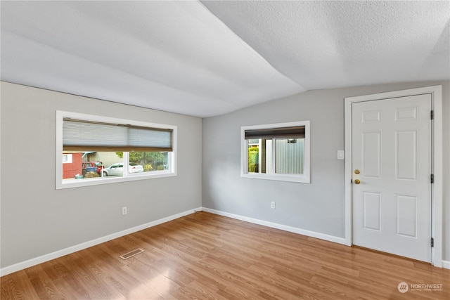 spare room with light wood-type flooring, lofted ceiling, and a wealth of natural light