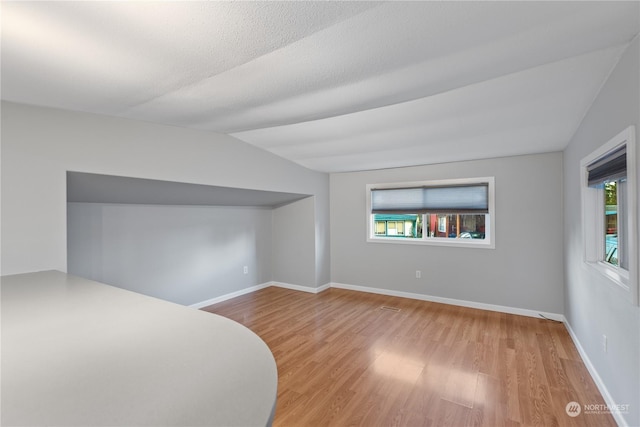 bonus room featuring a textured ceiling, light wood-type flooring, and lofted ceiling