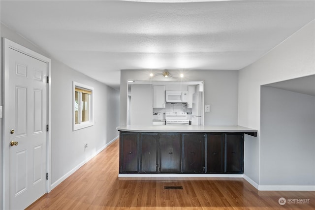 interior space with kitchen peninsula, a textured ceiling, white appliances, and light hardwood / wood-style floors