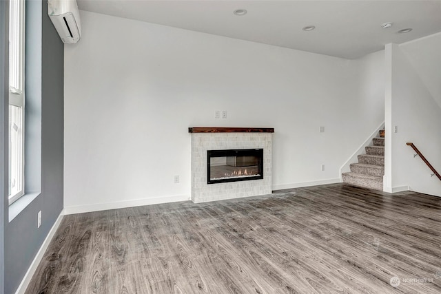 unfurnished living room featuring hardwood / wood-style flooring, an AC wall unit, and a tiled fireplace