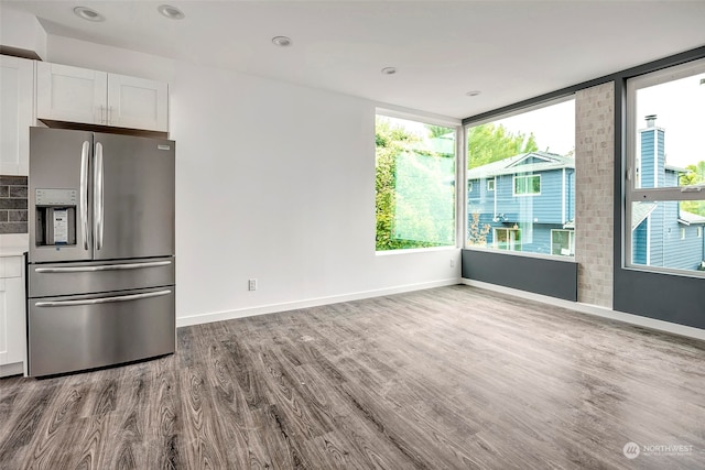 kitchen featuring stainless steel fridge with ice dispenser, light hardwood / wood-style floors, white cabinetry, and a wall of windows