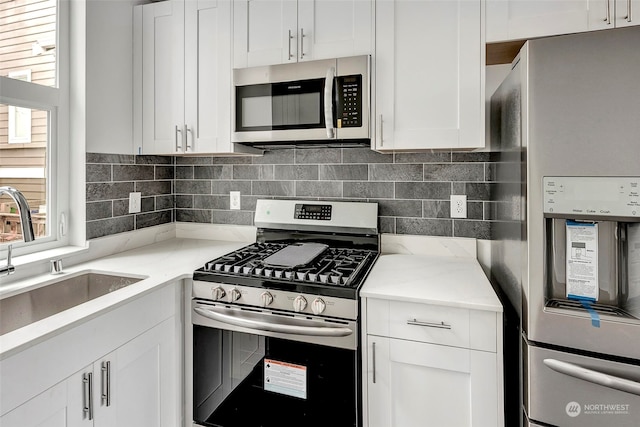 kitchen with sink, stainless steel appliances, light stone counters, backsplash, and white cabinets