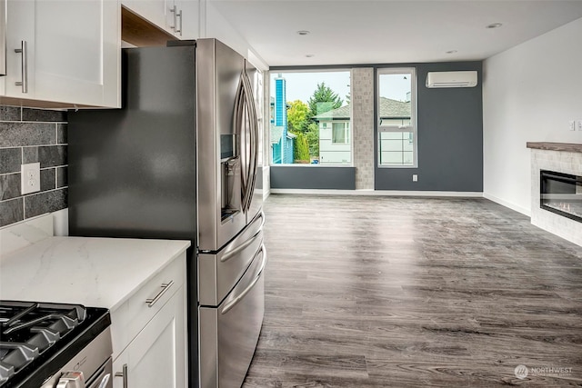 kitchen with stainless steel refrigerator with ice dispenser, a wall unit AC, decorative backsplash, white cabinets, and hardwood / wood-style flooring