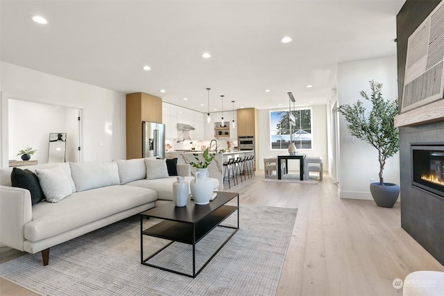 living room with a tile fireplace, sink, and light wood-type flooring