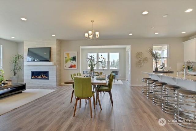 dining area with a fireplace, light hardwood / wood-style flooring, an inviting chandelier, and sink