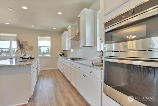 kitchen with light stone countertops, white cabinets, light hardwood / wood-style floors, and appliances with stainless steel finishes