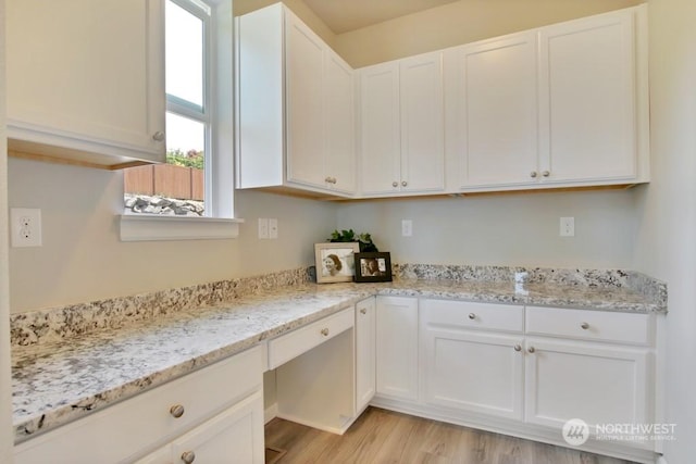 kitchen with white cabinets, light hardwood / wood-style flooring, and light stone counters