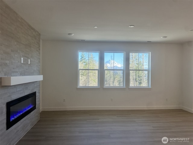 unfurnished living room featuring a large fireplace, plenty of natural light, baseboards, and wood finished floors