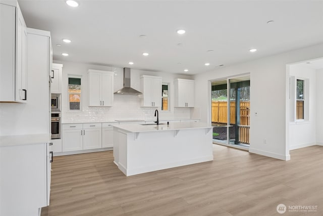 kitchen featuring backsplash, light countertops, stainless steel appliances, wall chimney exhaust hood, and a sink