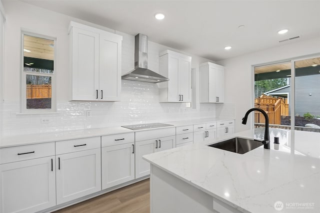 kitchen with light wood-style flooring, a sink, white cabinetry, wall chimney exhaust hood, and black electric cooktop