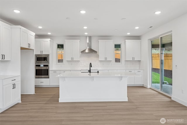 kitchen featuring light countertops, light wood-style floors, stainless steel appliances, wall chimney exhaust hood, and a sink