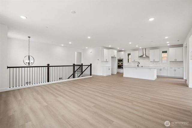 unfurnished living room with baseboards, recessed lighting, a sink, light wood-type flooring, and a chandelier